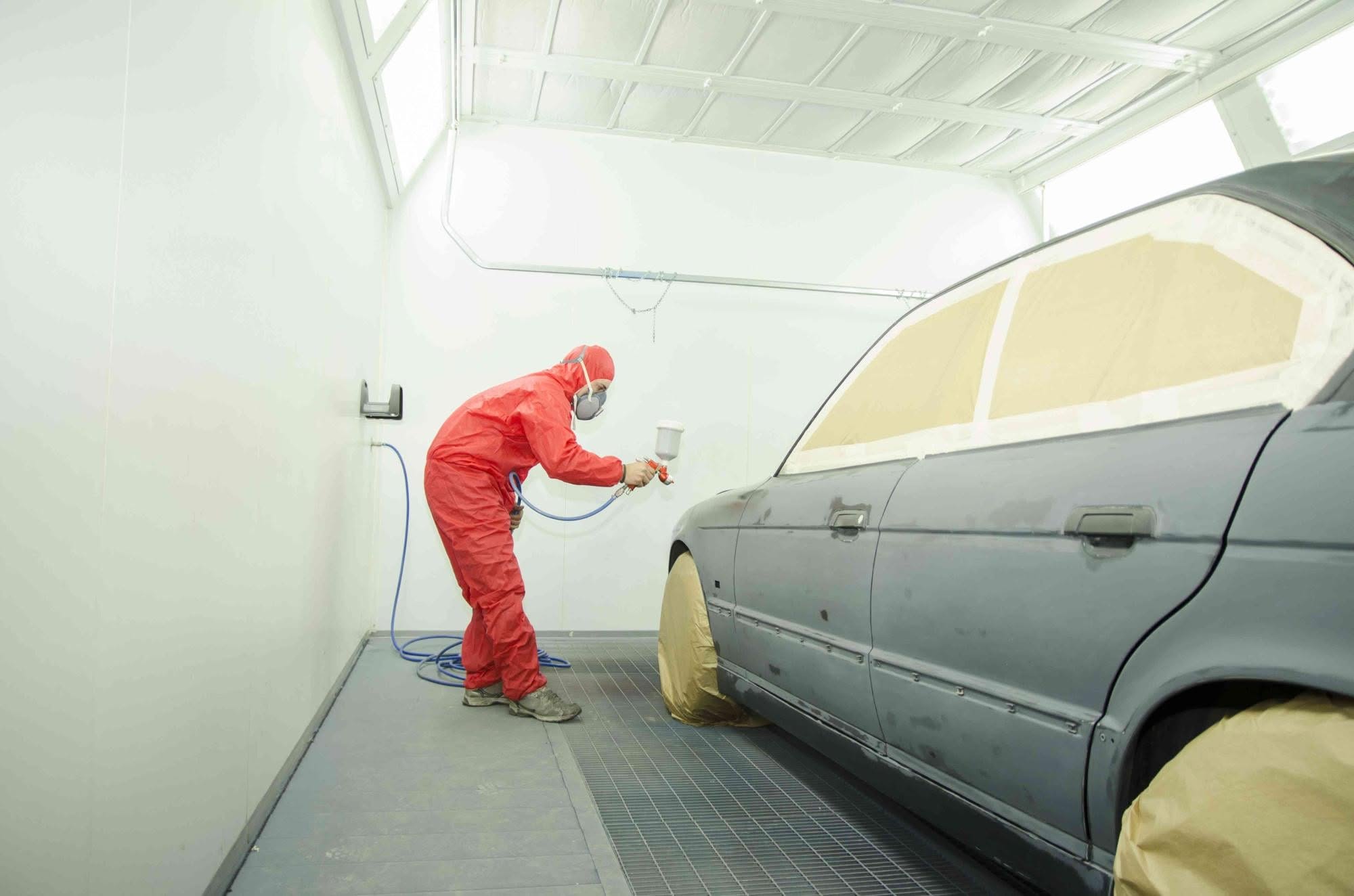 A spray painter working on a masked-up car inside the booth